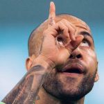 Na imagem Daniel Alves aparece em gesto apontando o dedo para o céu com o olho lacrimejando