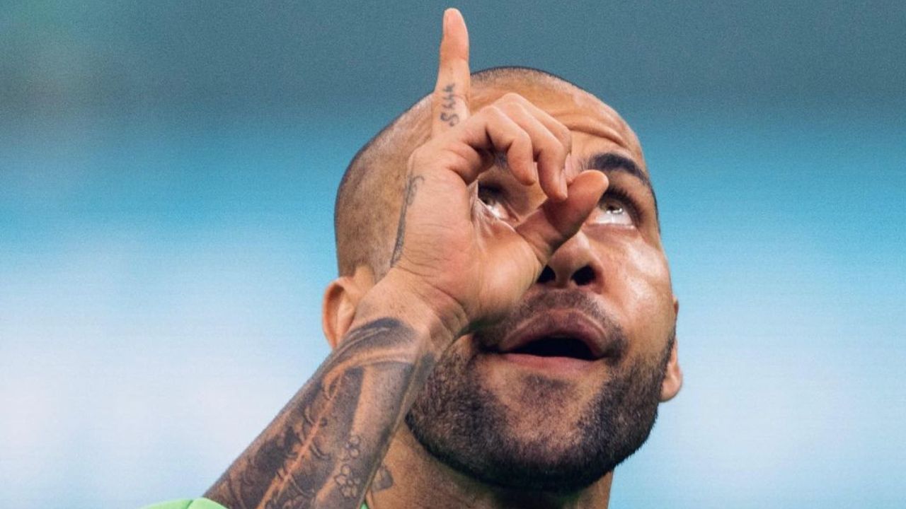 Na imagem Daniel Alves aparece em gesto apontando o dedo para o céu com o olho lacrimejando