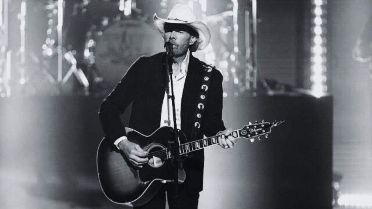 Músico country Toby Keith aparece em cima do palco cantando e tocando violão durante show