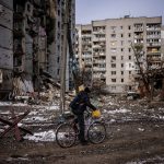 Ciclista na frente de destroços deixados por ataques russos na Ucrânia