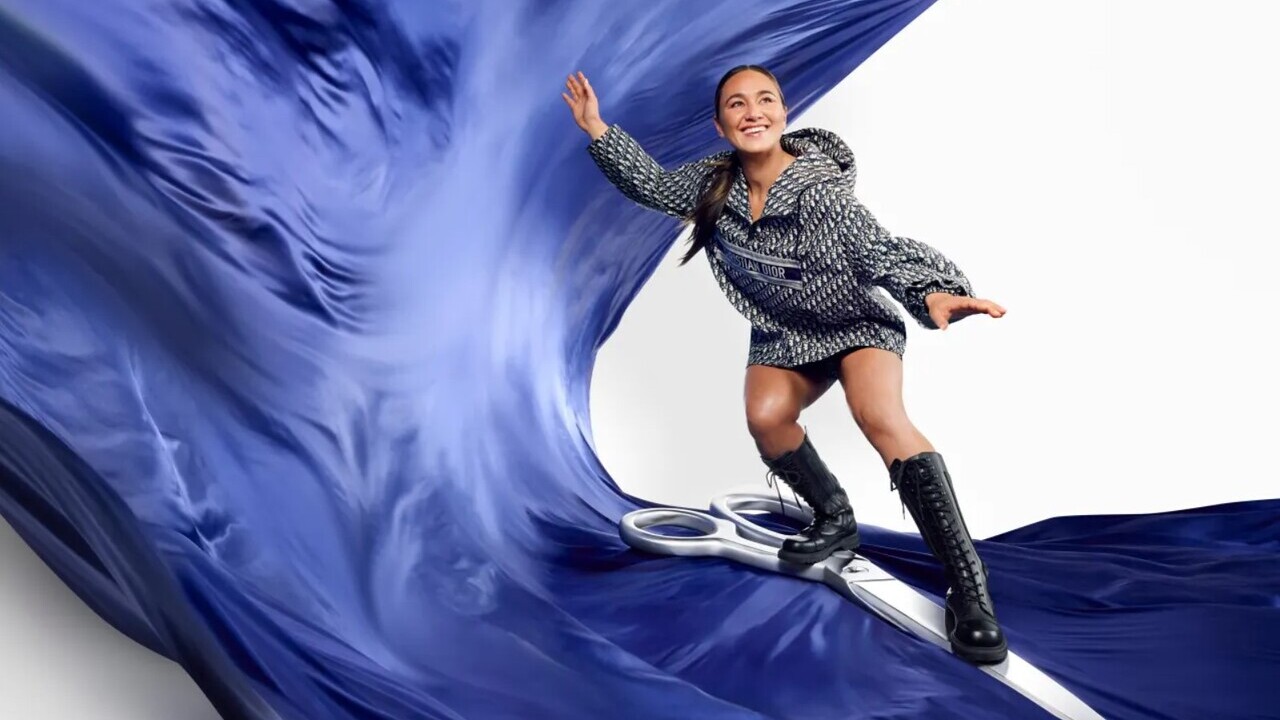 Carissa Moore, vestida em traje preto e branco da Dior, posa em cima de tesoura gigante e tecido azul, como se estivesse surfando.