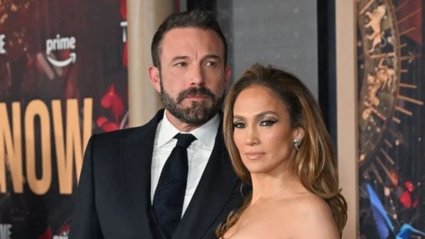 Jennifer Lopez e Ben Affleck durante evento. Ben veste um terno preto e uma camisa branca com gravata preta. Jennifer está com um vestido preto sem mangas.