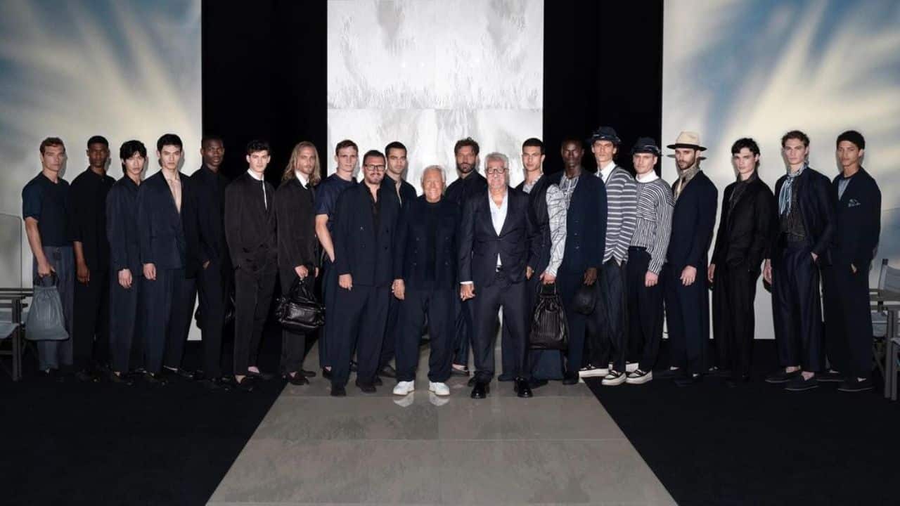 Giorgio Armani com modelos para o desfile de nova coleção. Roupas consistem em diversos estilos de alfaiataria em tons de cinza e preto.