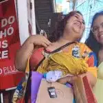 Duas mulheres posam para uma placa vermelha escrita "Feira do brechó plus size POPlus"