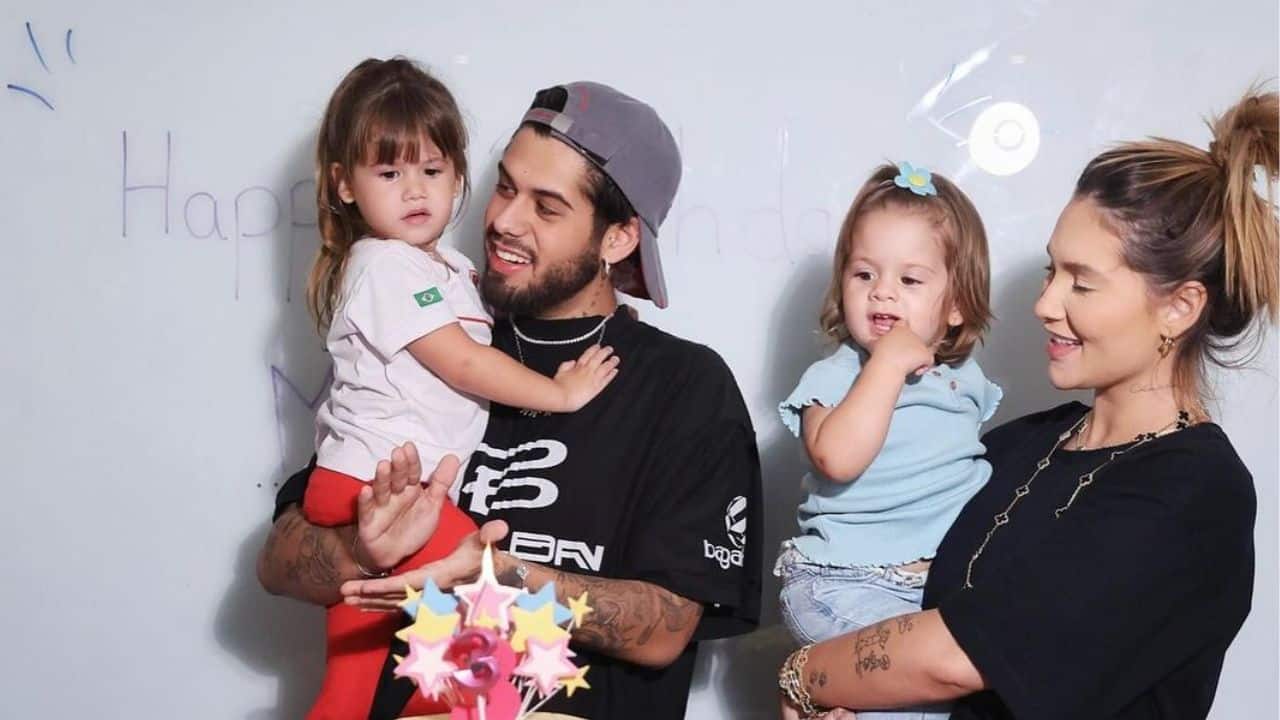 Virginia veste preto e está segurando Maria Flor, que veste azul. Zé Felipe, também vestido de preto e boné, segura Maria Alice nos braços. Ela veste uma blusa branca e calça vermelha. Os quatro estão de frente a uma parede branca