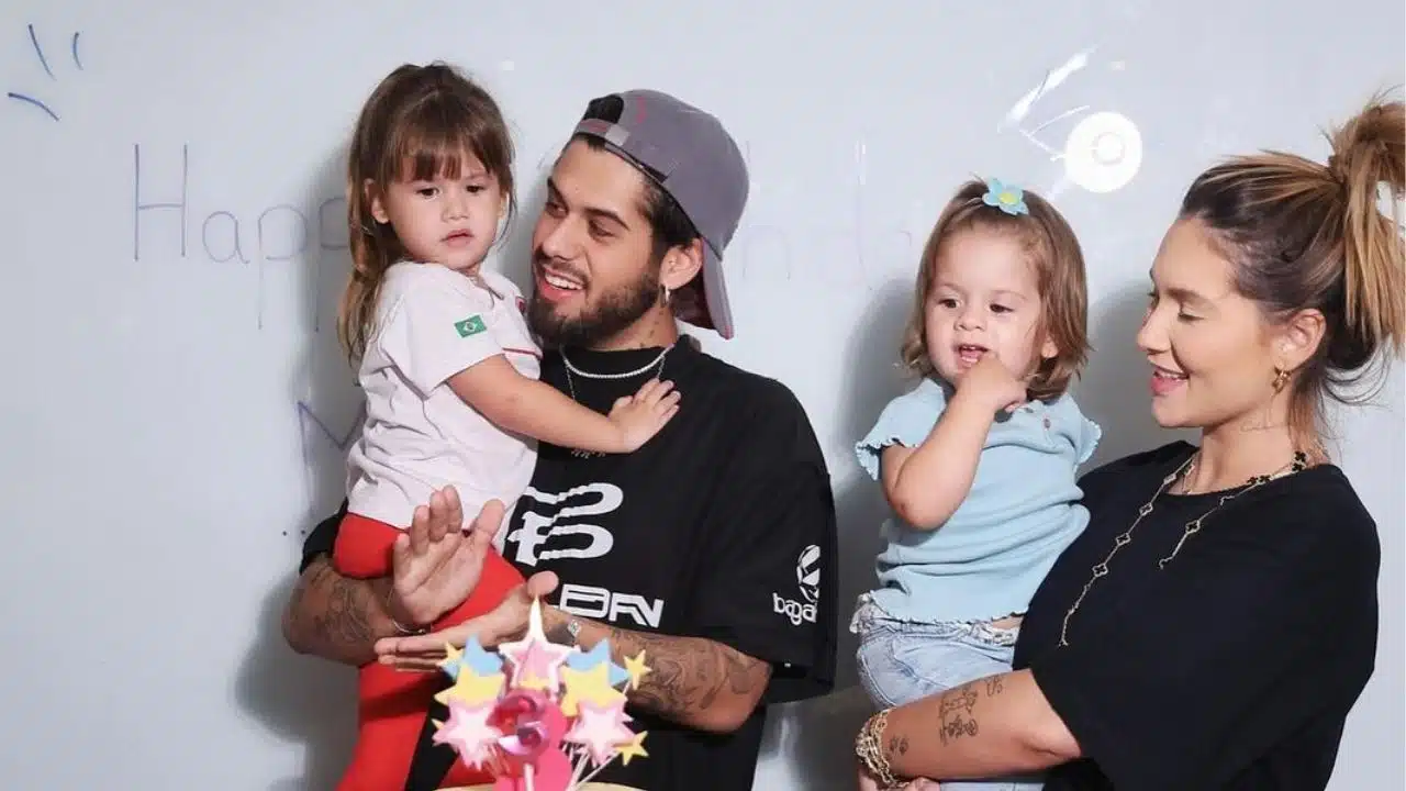 Virginia veste preto e está segurando Maria Flor, que veste azul. Zé Felipe, também vestido de preto e boné, segura Maria Alice nos braços. Ela veste uma blusa branca e calça vermelha. Os quatro estão de frente a uma parede branca