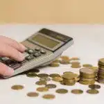 Mão mezendo na calculadora e moedas na mesa