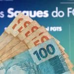 Notas de 100 e 50 reais em frente a um banner informativo sobre os novos saques do FGTS