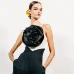 Modelo usando um elegante vestido preto e branco com uma grande flor preta em destaque no busto, desfilando na Semana de Moda de Nova York