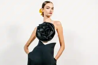 Modelo usando um elegante vestido preto e branco com uma grande flor preta em destaque no busto, desfilando na Semana de Moda de Nova York