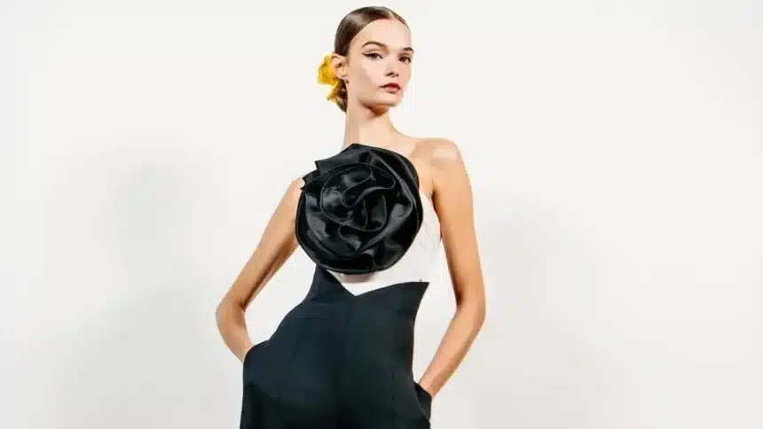 Modelo usando um elegante vestido preto e branco com uma grande flor preta em destaque no busto, desfilando na Semana de Moda de Nova York