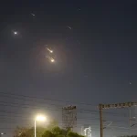 Mísseis iluminam o céu noturno sobre Tel Aviv, com várias explosões visíveis, enquanto o sistema de defesa antimísseis tenta interceptá-los