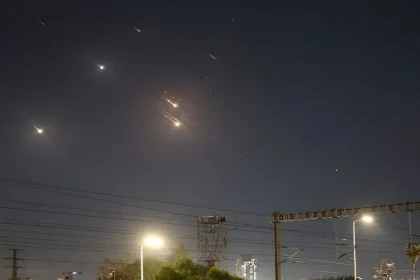 Mísseis iluminam o céu noturno sobre Tel Aviv, com várias explosões visíveis, enquanto o sistema de defesa antimísseis tenta interceptá-los