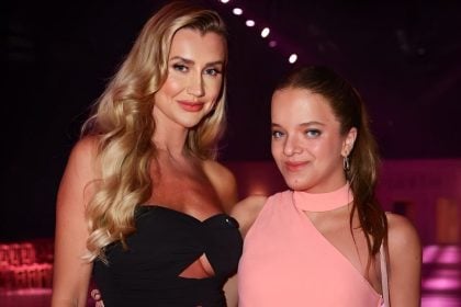 Duas mulheres posando em evento de moda, uma com vestido preto e outra com vestido rosa