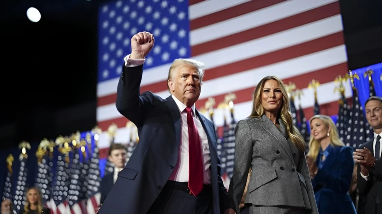 Donald Trump, ao lado de sua esposa Melania Trump, ergue o punho em sinal de vitória, com a bandeira dos Estados Unidos ao fundo, durante o discurso de celebração por sua reeleição à presidência