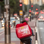 Entregador de aplicativo pedalando em ciclovia movimentada em São Paulo, com mochila térmica do iFood