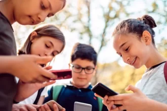 Foto mostrando grupo de crianças com celulares na mão, ocasião que a sociedade busca combater cada vez mais, devido aos prejuizos científicamente comprovados que o aparelho causa na vida e na formação dos jovens