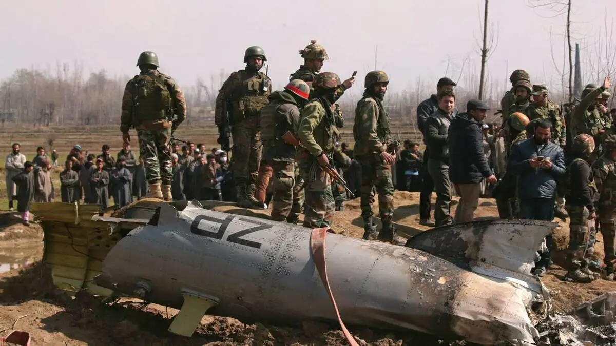Soldados da Índia ao lado de destroços de helicóptero das suas forças aéreas na Caxemira; ao redor, moradores observam dia de tensões 