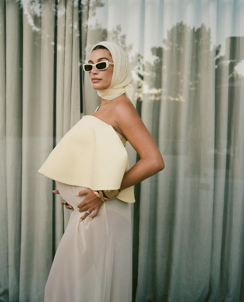 Hailey Bieber abre o jogo ao falar sobre família com Justin Uma mulher branca com um vestido bege claro e óculos escuro ostentando uma barriga de gravidez