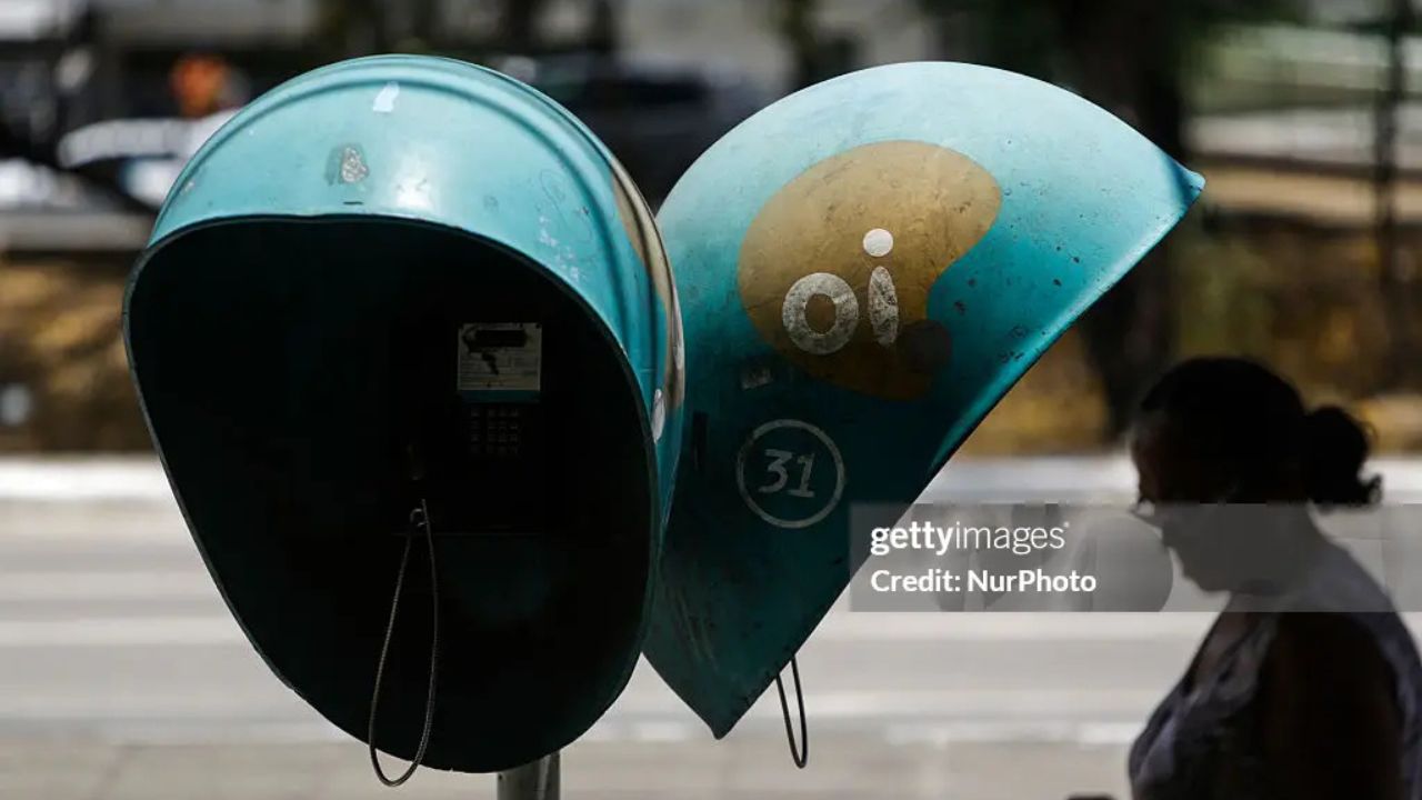 Imagem de dois orelhões da Oi e uma senhora passando na frente
