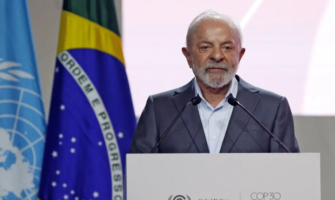 Presidente Lula na frente de duas bandeiras, uma do Brasil e outra da ONU