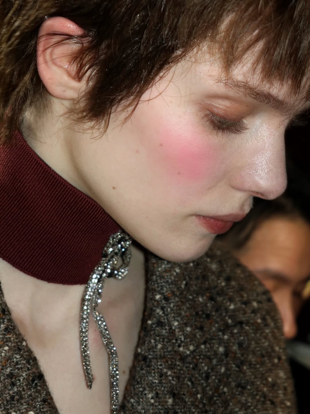 Close-up de modelo nos bastidores da NYFW, com blush rosado intenso nas bochechas, pele iluminada e maquiagem minimalista, destacando tendências de beleza da temporada.