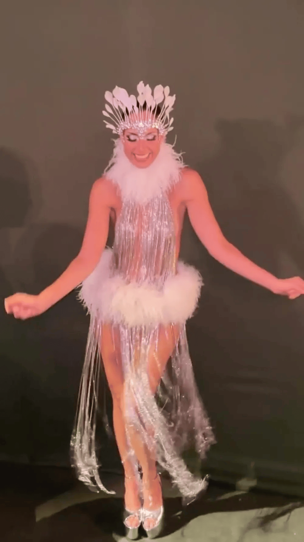 Camila Pitanga surge com dois looks luxuosos e rouba a cena no Baile do Copa Atriz Camila Pitanga usa figurino prateado com franjas longas e brilhantes, gola e detalhe na cintura em plumas brancas, além de adorno de cabeça com penas claras, enquanto posa sorrindo em fundo escuro
