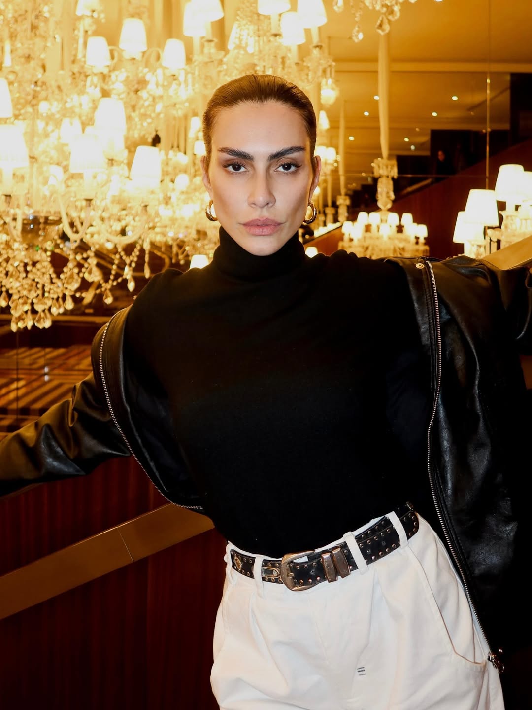 Cleo Pires com cabelo preso, blusa preta de gola alta e calça branca