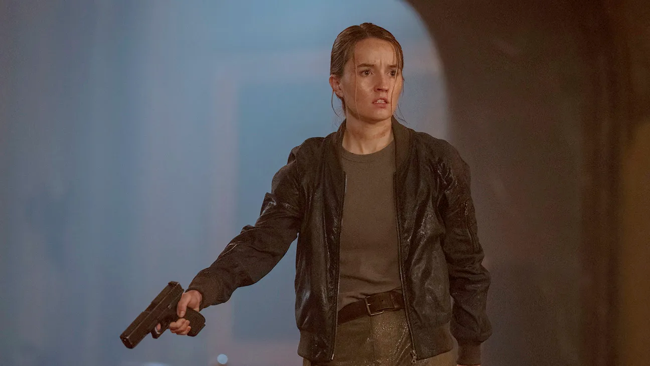 Kaitlyn Dever como Abby em The Last of Us. Atriz branca de cabelos castanhos empunhando uma pistola.
