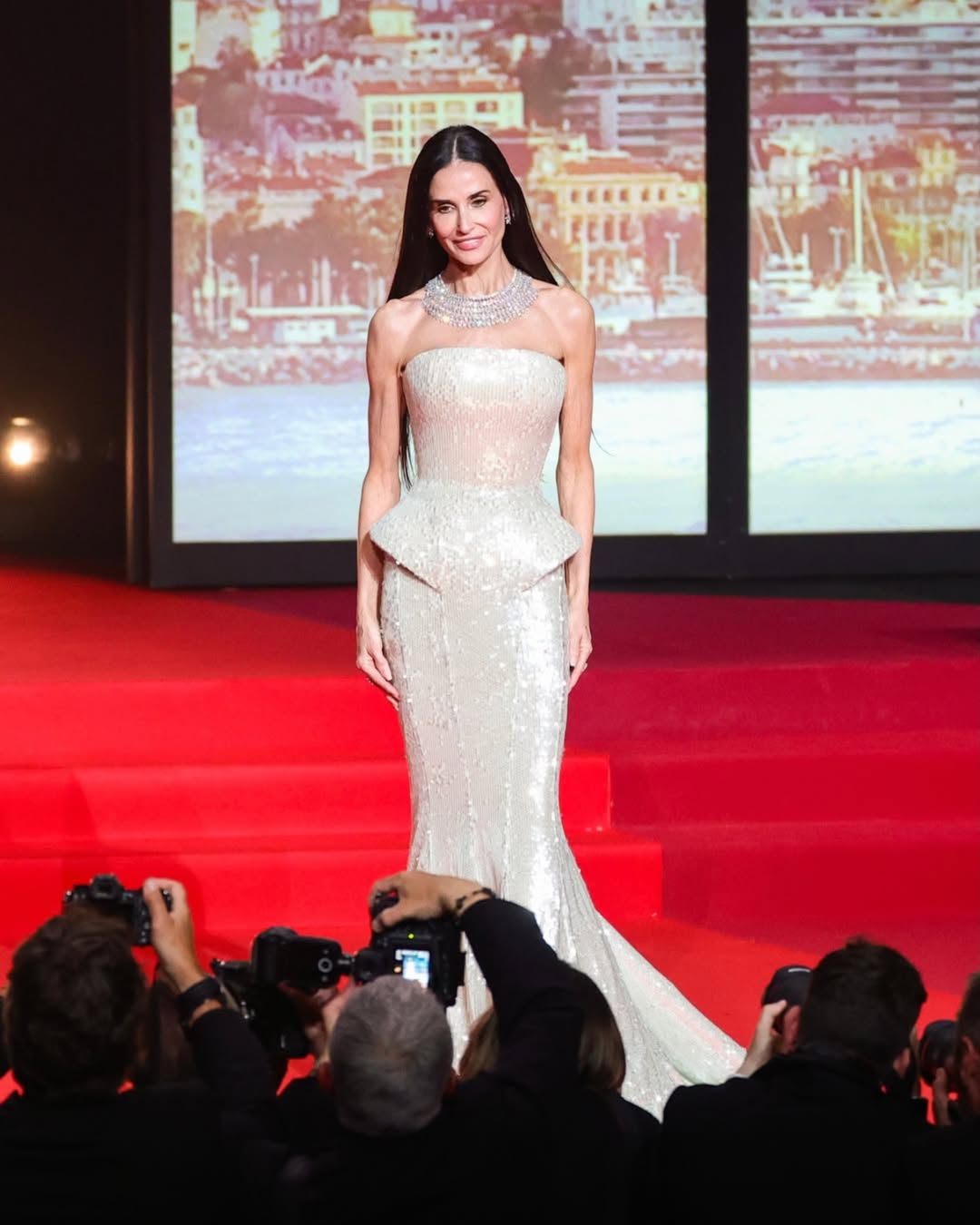 Demi Moore, mulher branca de cabelos pretos, que usa vestido prateado em tapete vermelho