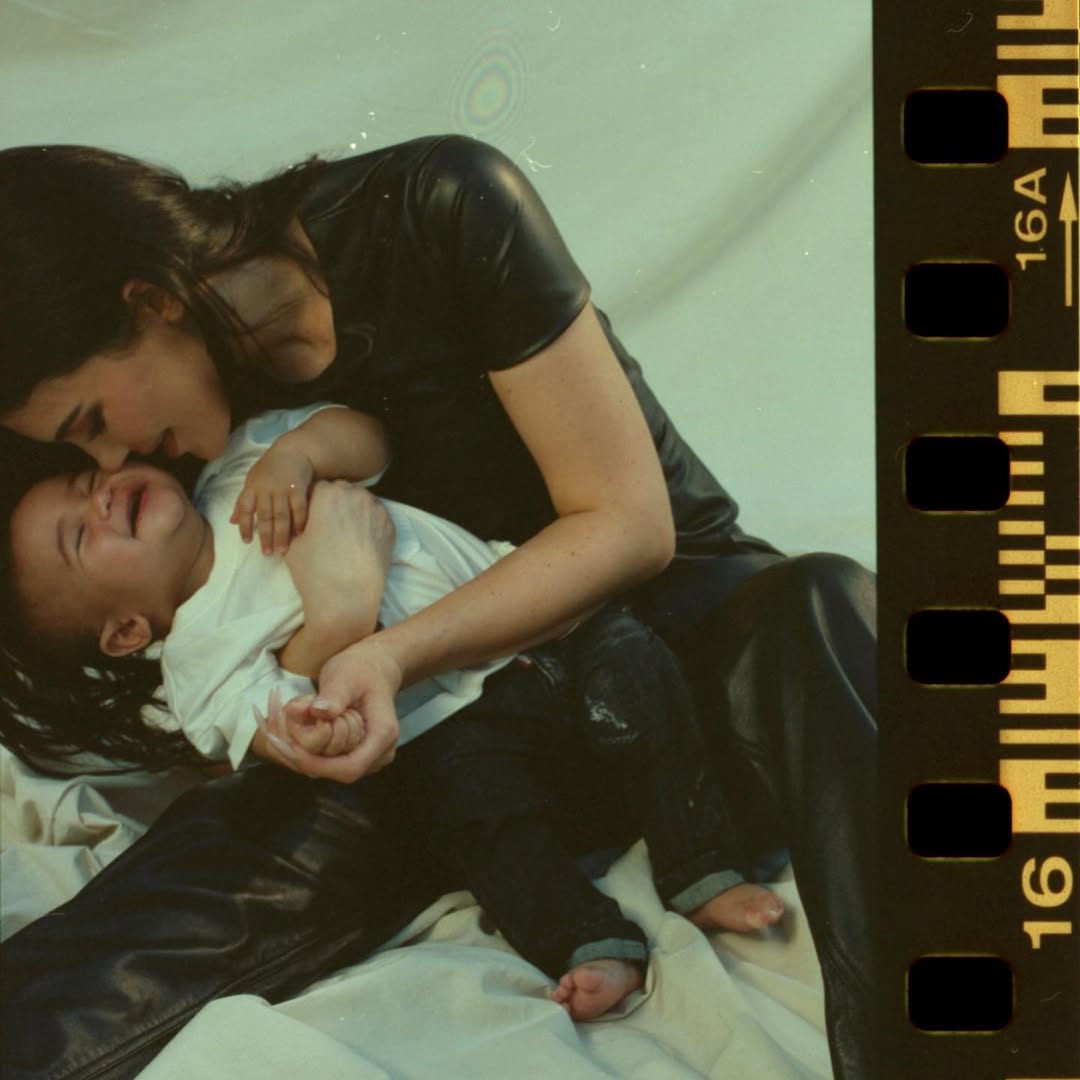 Kylie Jenner, mulher branca de cabelos cor castanho escuro, abraçada com filho bebê Aire