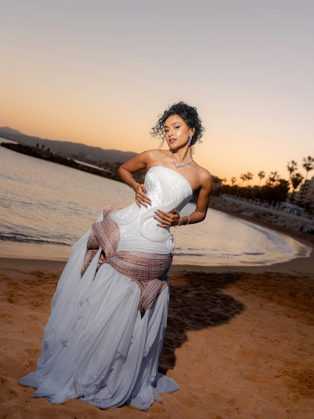 Rida Tharana, mulher que usa cabelo preso em coque e vestido branco com detalhes rosê e estrutura de corset na parte superior