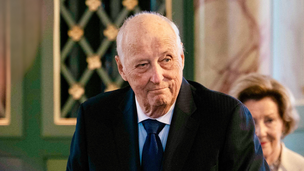 Foto do rei Harald V usando um terno preto e gravata azul durante um compromisso.