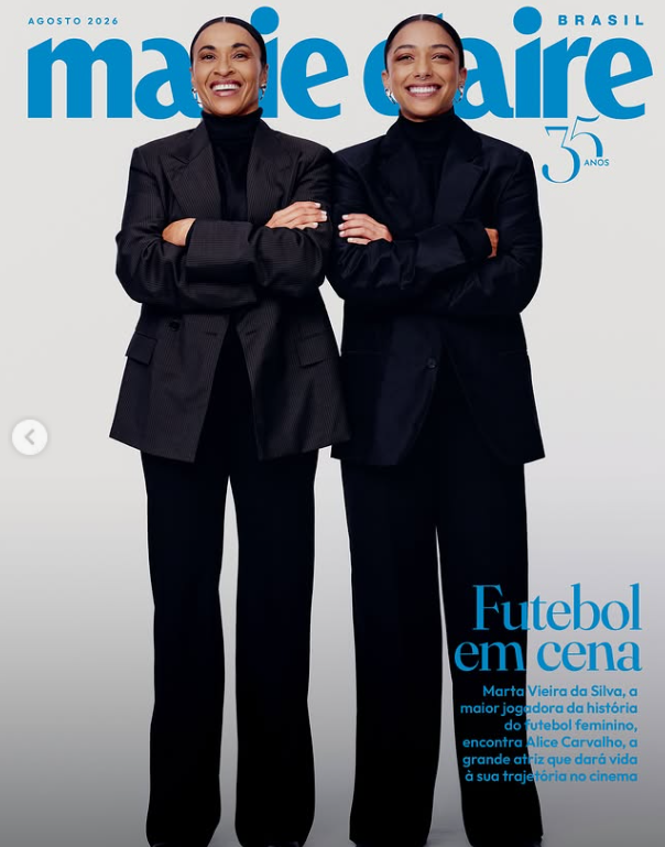Duas mulheres, de preto, olhando para frente. Ambas estão lado a lado e de braços cruzados. 