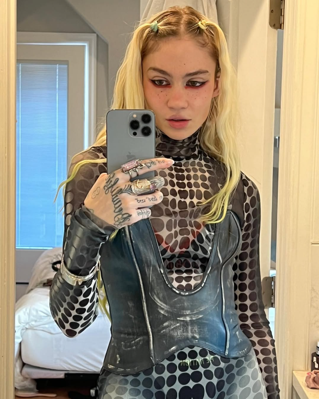 Mulher branca, loira, segura o telefone para tirar uma selfie. 